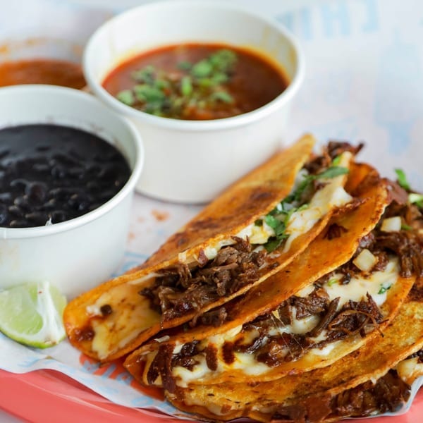 Chido Taco's birria tacos with melted cheese, cilantro, lime, and sides of consome and black beans.