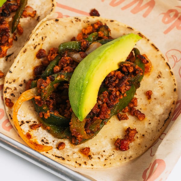 A Chido Taco with chorizo, green peppers, onions, and a slice of avocado on a corn tortilla.