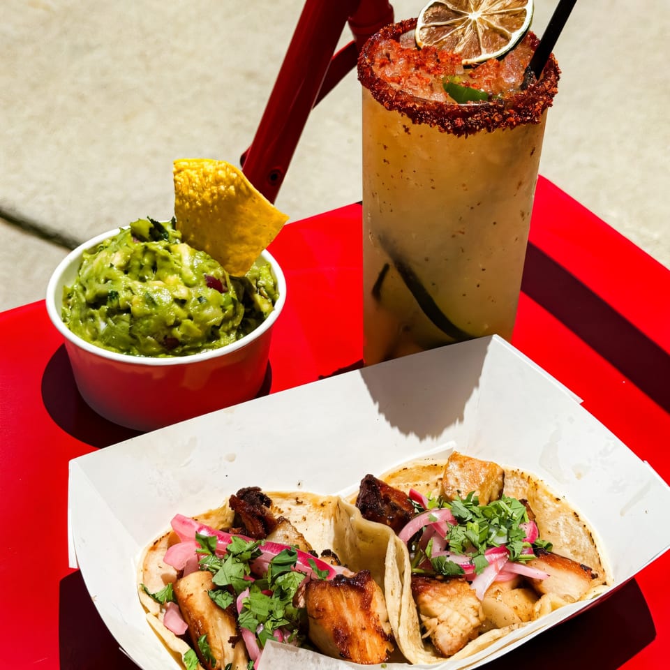 Chido Taco's guacamole, tacos with pork belly, and a chili-rimmed margarita on a red table.