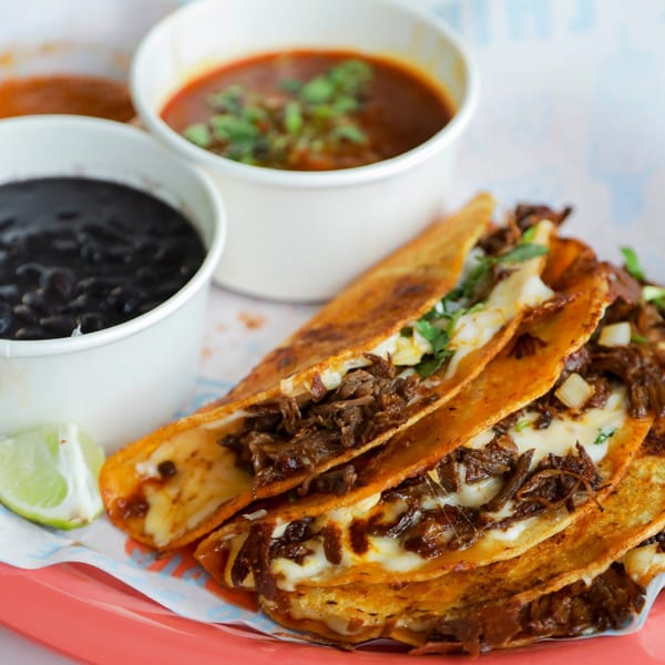 Chido Taco's birria tacos with melted cheese, a side of black beans, and a cup of consommé.