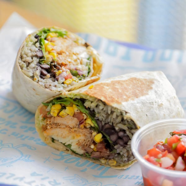 Two Chido Taco burritos, cut in half, revealing chicken, rice, black beans, corn, and salsa.