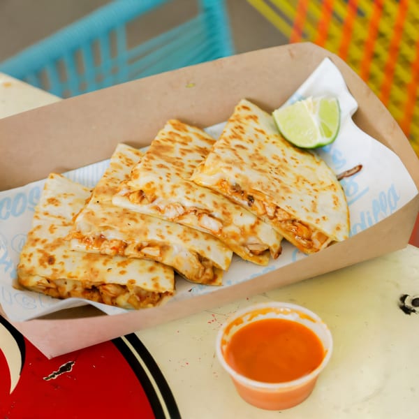 Chido Taco's quesadillas in a cardboard tray with a lime wedge and a side of red sauce.