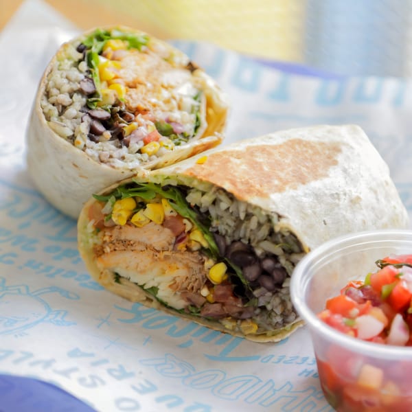 Two Chido Taco burritos, one cut in half, revealing chicken, rice, beans, corn, and salsa.