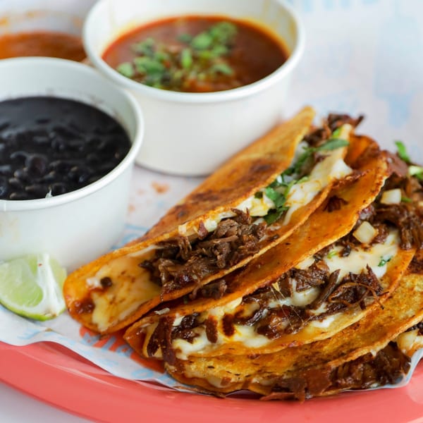 Chido Taco's birria tacos with melted cheese, cilantro, onions, and lime, served with black beans and consommé.