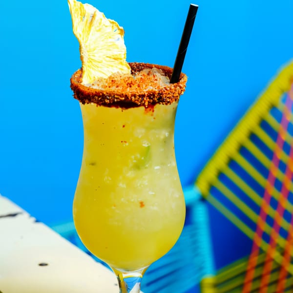 A Chido Taco pineapple margarita with a chili-lime rim and dried pineapple garnish against a blue background.