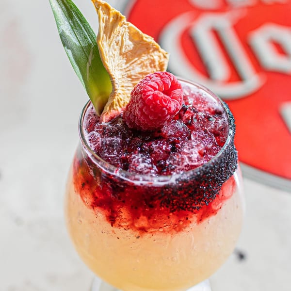 A Chido Taco raspberry margarita with a black salt rim, dried pineapple, and green leaf garnish.