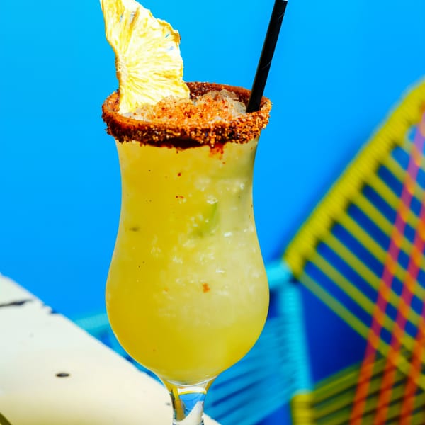 A Chido Taco pineapple margarita with a chili-lime rim and dried pineapple garnish against a blue background.