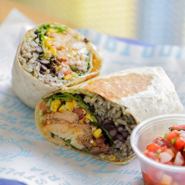Two Chido Taco burritos, cut in half, revealing chicken, rice, beans, corn, and lettuce, with a side of salsa.