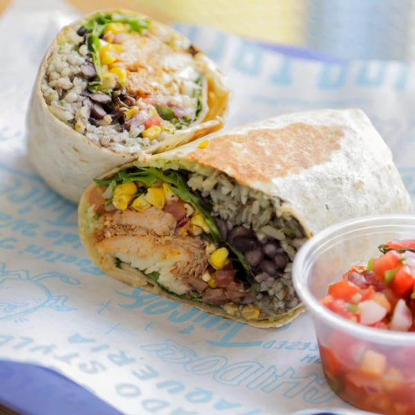 Two Chido Taco burritos, cut in half, revealing chicken, rice, beans, corn, and salsa.