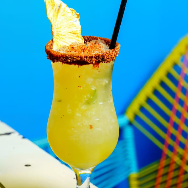 A Chido Taco pineapple margarita with a chili-lime rim and dried pineapple garnish against a blue background.