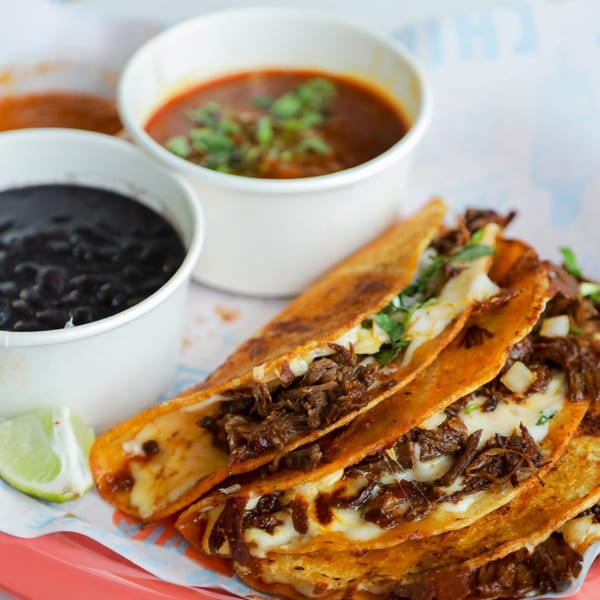 Chido Taco birria tacos with melted cheese, shredded beef, cilantro, onions, and sides of consome and black beans.