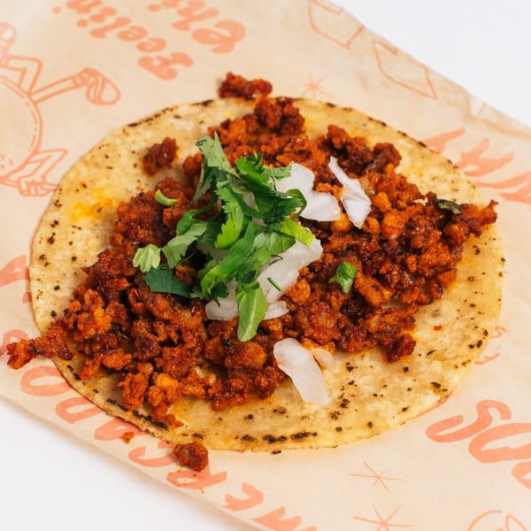 Chido Taco's al pastor taco, topped with cilantro and diced onions, on branded paper.